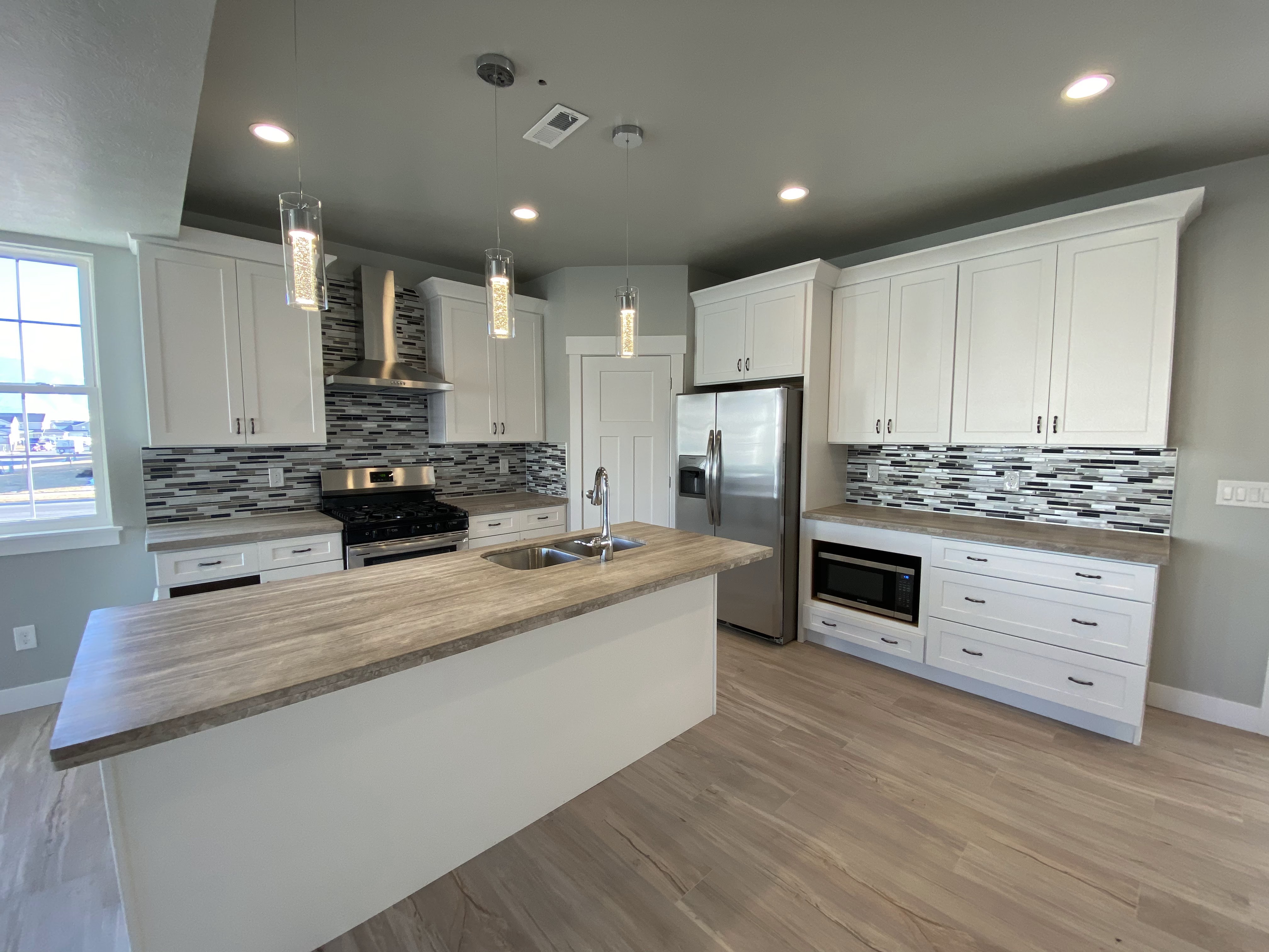 Bright kitchen with white cabinetry, warm counters, and pendant lighting
