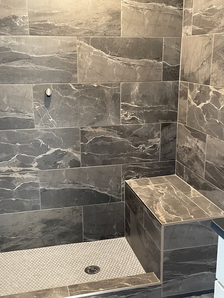 Large shower with dark stone tile and a built in bench