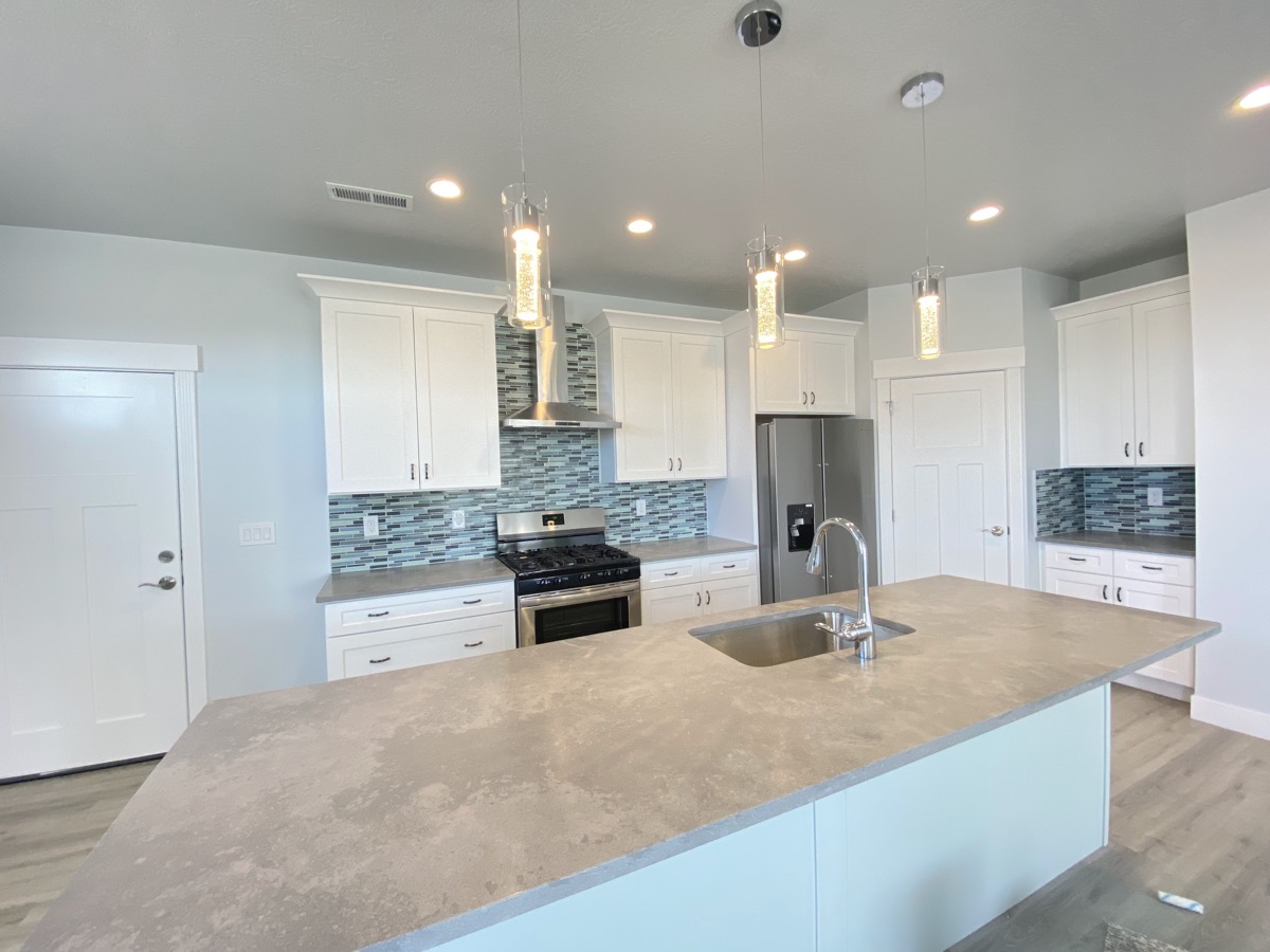 White kitchen with a large stone island and glass pendants